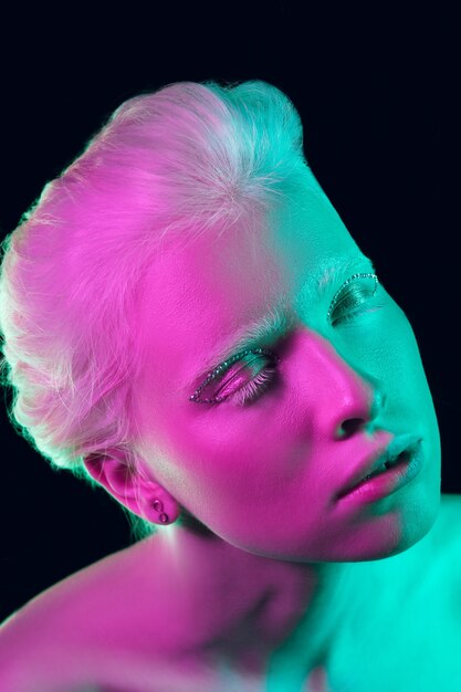 Menina albina com pele branca, lábios naturais e cabelo branco em luz de néon, isolado no fundo preto do estúdio.