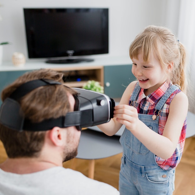 Menina alegre, ajudando o pai com fone de ouvido de vr