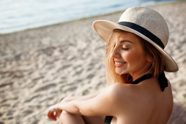 Menina alegre bonita no chapéu baseia-se na praia de manhã