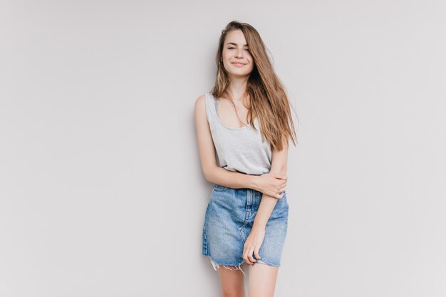 Menina alegre com cabelo castanho claro posando. Foto interna de uma espetacular senhora caucasiana em saia jeans sorrindo