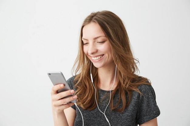 Menina alegre feliz sorrindo olhando para a tela do telefone ouvindo streaming de música.