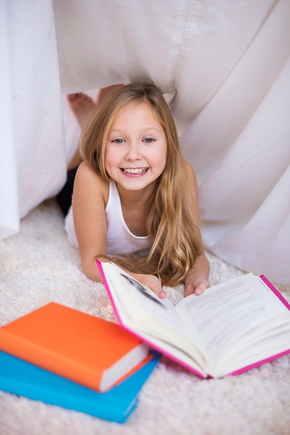 Menina alegre lendo livro em um abrigo feito à mão