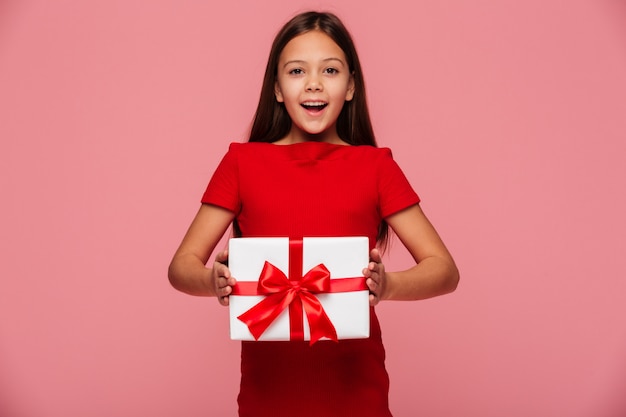 Menina alegre, mostrando o presente e sorrindo isolado sobre rosa