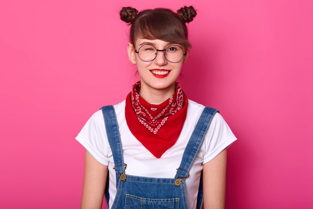 Menina alegre positiva energética nova que está isolada sobre o rosa no estúdio, tendo um olho fechado