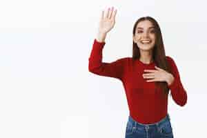 Foto grátis menina alegre vê amigo na multidão tentando atrair a atenção enquanto acena com a mão levantada em olá ou oi gesto dizer aqui como sorrindo e pulando para ser visto em pé fundo branco alegre