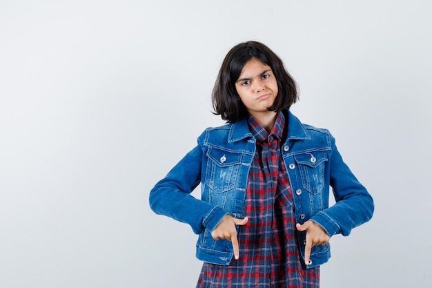 Menina apontando para baixo na camisa, jaqueta e parecendo hesitante. vista frontal.