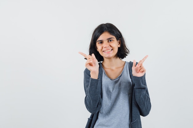 Menina apontando para cima com camiseta, jaqueta e parecendo alegre