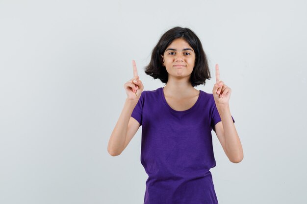 Menina apontando para cima em t-shirt e parecendo confiante.