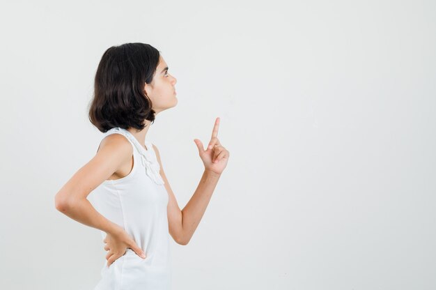 Menina apontando para cima na blusa branca e olhando com foco. .