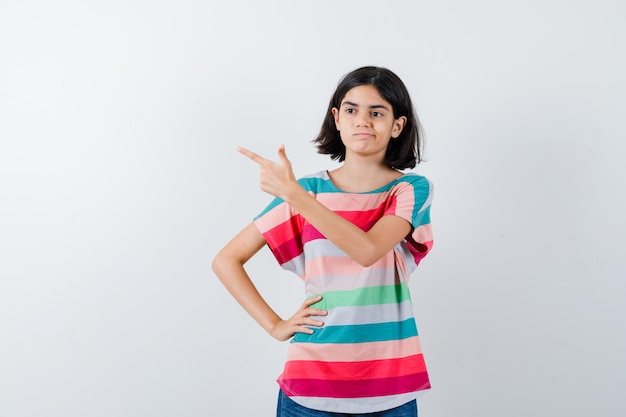 Foto grátis menina apontando para o canto superior esquerdo da camiseta e olhando pensativa. vista frontal.