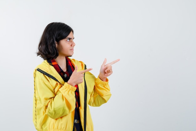 Menina apontando para o lado direito com camisa xadrez, jaqueta e parecendo confiante