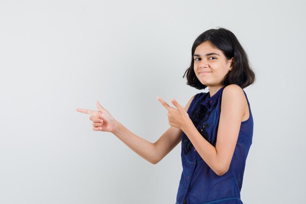 Menina apontando para o lado esquerdo com blusa azul e parecendo brincalhona