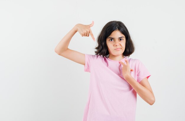 Menina apontando para si mesma em uma camiseta rosa e parecendo confusa. vista frontal.