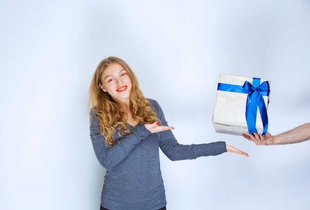 Menina apontando uma caixa de presente azul branca oferecida a ela.