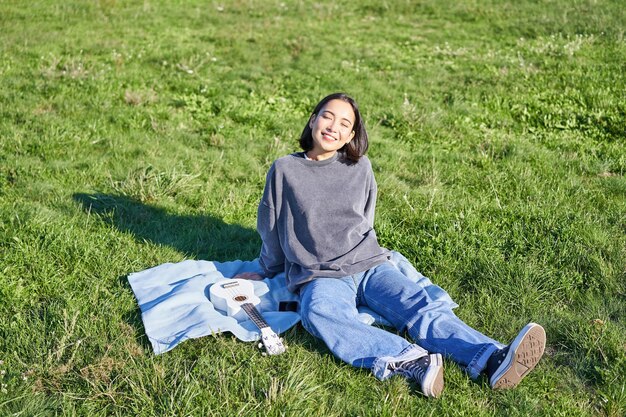 Menina asiática aproveitando o dia ensolarado ao ar livre estudante feliz fazendo piquenique na grama no parque jogando no reino unido