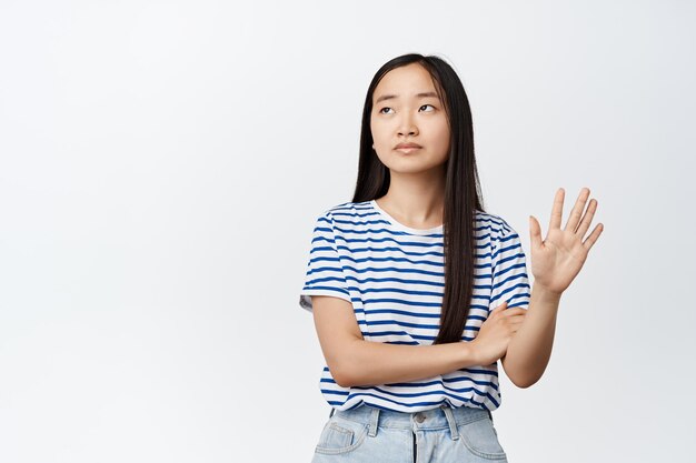 Menina asiática arrogante sem diversão, mostrando um gesto com a mão olhando para longe com antipatia, recusando algo mostrar sinal de rejeição fundo branco