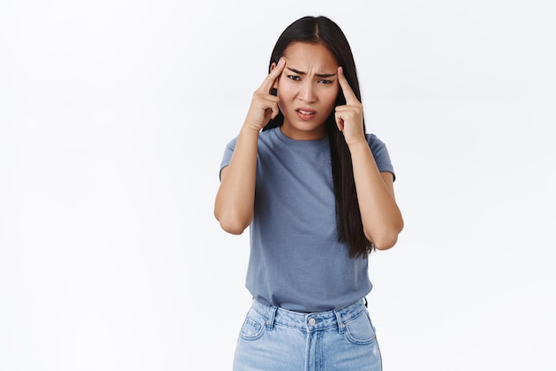 Menina asiática bonita doente problemática com corte de cabelo longo escuro franzindo a testa perplexo ou angustiado sentindo-se desconfortável e indeciso não consigo pensar em uma boa ideia para o projeto sofre de dor de cabeça ou enxaqueca toque templos