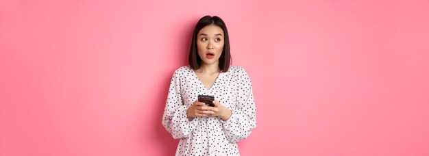 Foto grátis menina asiática confusa de compras on-line segurando smartphone parecendo sem noção no canto superior esquerdo