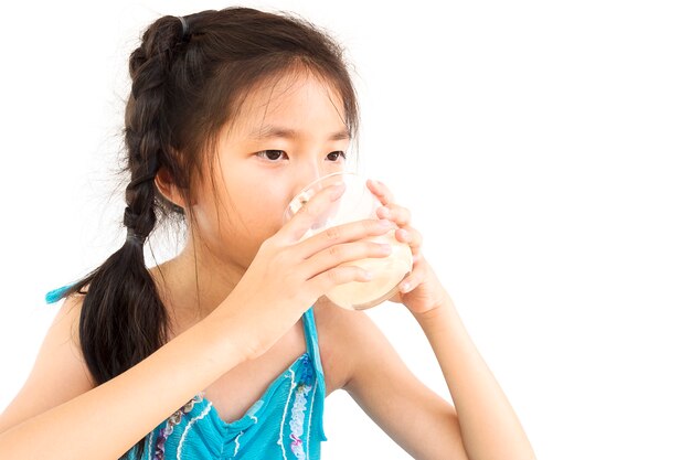 Menina asiática está bebendo um copo de leite sobre fundo branco