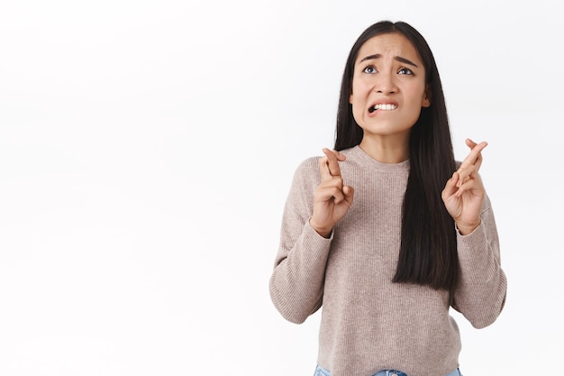 Menina asiática fofa preocupada e preocupada em uma blusa bege, preocupada, cruze os dedos, boa sorte, mordendo o lábio nervosamente, olhe para o gráfico, esperando resultados importantes, ansiosamente espero que o desejo se torne realidade