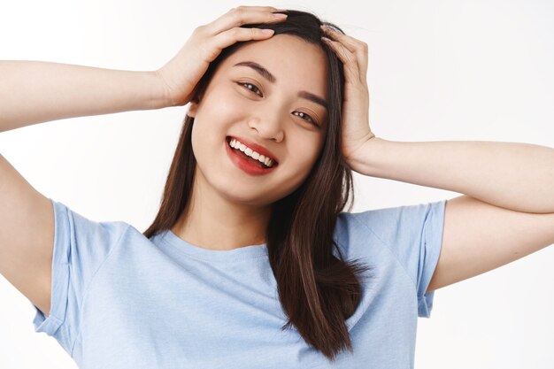 Menina asiática linda morena despreocupada otimista tendo maravilhosas férias de verão, divirta-se toque a cabeça despreocupada extremamente positiva, humor alegre, sorrindo, câmera