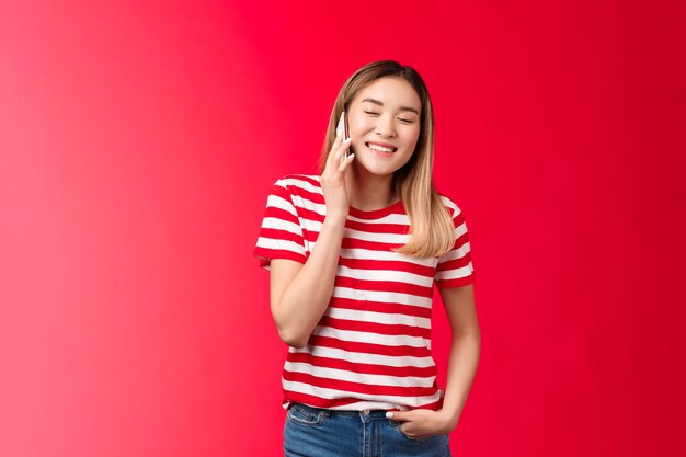 Menina asiática loira simpática despreocupada tendo uma conversa engraçada falando de telefone feche os olhos jo ...