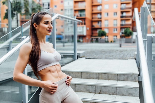 Menina atlética com abs no parque após o treino relaxar. Mulher bonita do esporte.