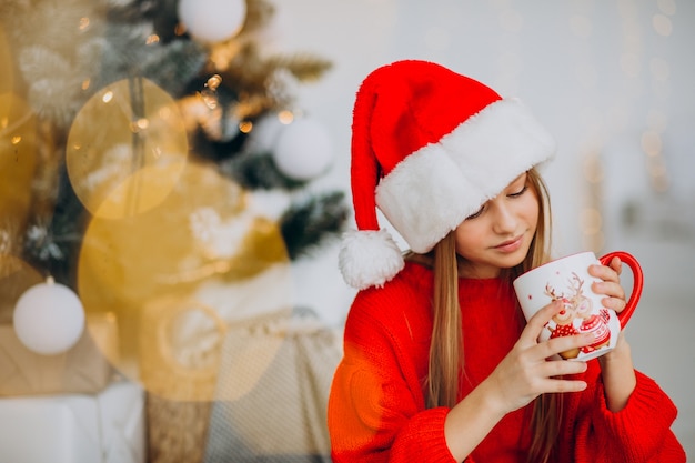 Menina bebendo chocolate perto da árvore de natal