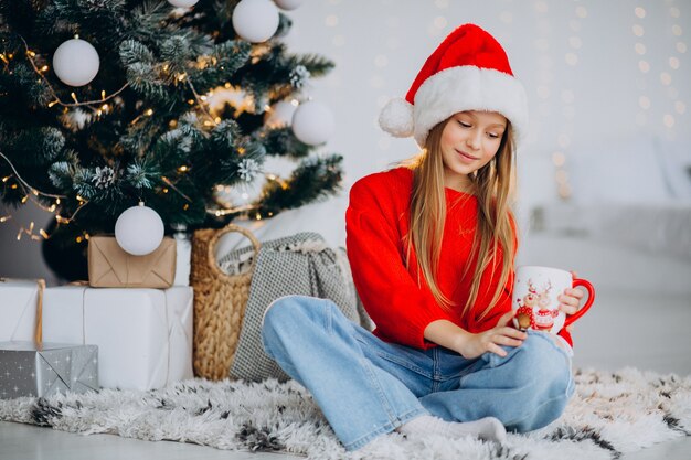 Menina bebendo chocolate perto da árvore de natal