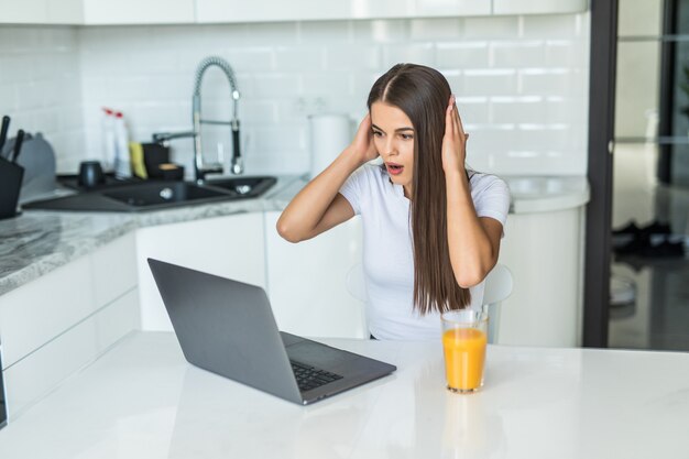 Menina bonita animada chocado jovem estudante sentado dentro de casa usando o computador portátil