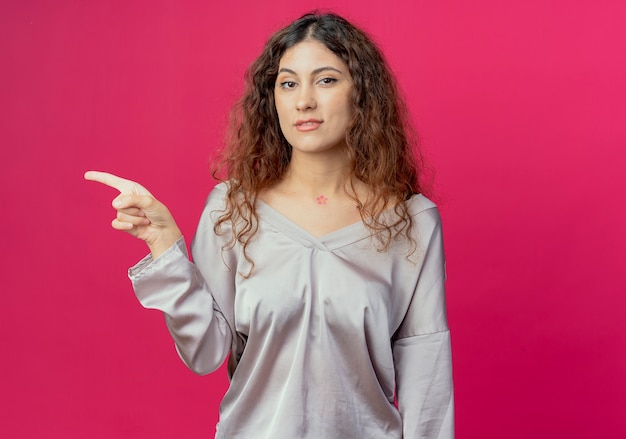 Foto grátis menina bonita apontando para o lado isolado na parede rosa com espaço de cópia