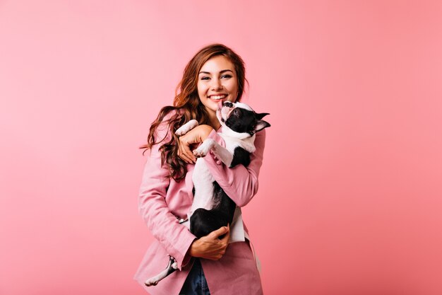 Menina bonita branca segurando bulldog e rindo. Mulher caucasiana alegre com cachorro se divertindo.