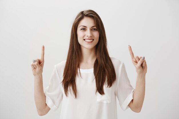 Menina bonita caucasiana feliz apontando os dedos para cima e sorrindo satisfeita