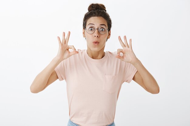 Menina bonita com óculos posando contra a parede branca