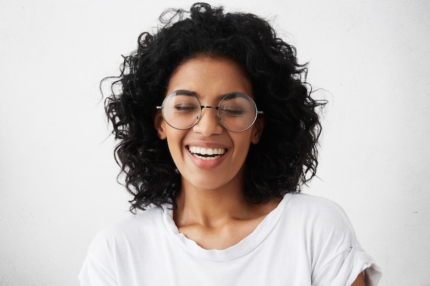 Menina bonita com pele escura e limpa e um lindo sorriso cheio de dentes rindo alto de uma piada engraçada