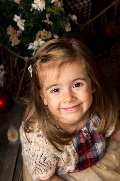 Menina bonita com um brinquedo Papai Noel nas mãos senta-se sobre um piso de madeira com decoração de Natal
