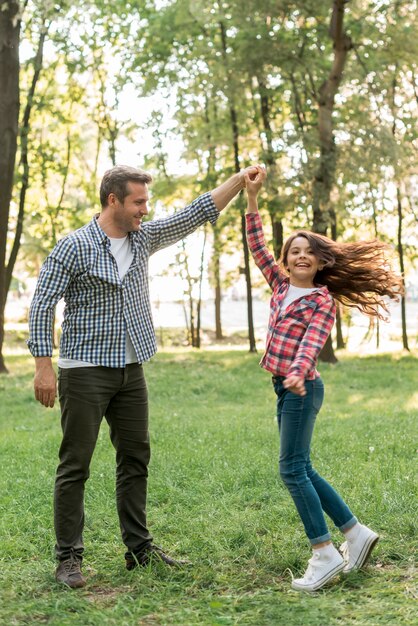 Menina bonita dançando com o pai na terra gramada no parque