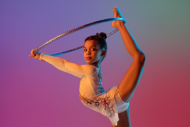 Menina bonita de ginasta rítmica afro-americana praticando em fundo de estúdio gradiente em luz neon