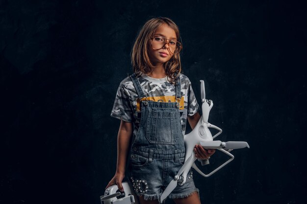 Menina bonita de óculos está posando para o fotógrafo no estúdio escuro enquanto segura o controlador e o drone.