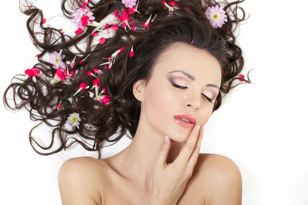 Menina bonita, deitado com flores vermelhas brilhantes em sua maquiagem brilhante cabelo isolada no branco