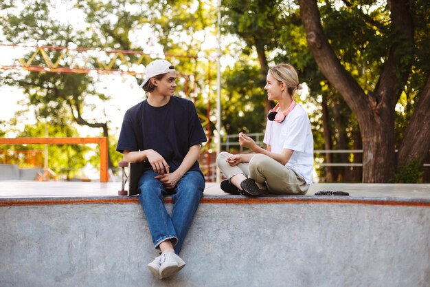 Menina bonita e jovem conversando alegremente enquanto passam tempo juntos no skatepark moderno