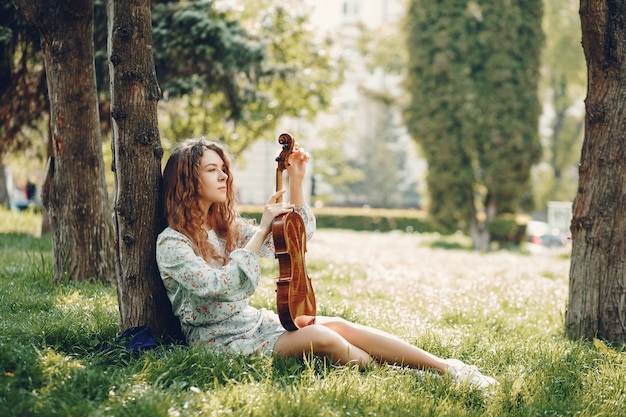 Menina bonita em um parque de verão com um violino