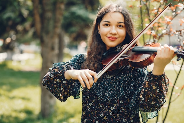 Menina bonita em um parque de verão com um violino