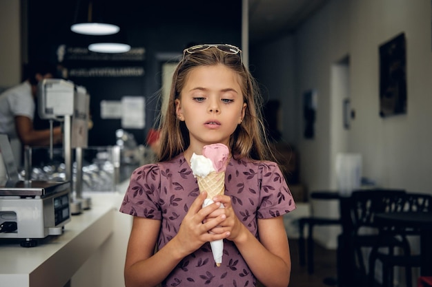 Menina bonita em um vestido, comendo sorvete em um café.