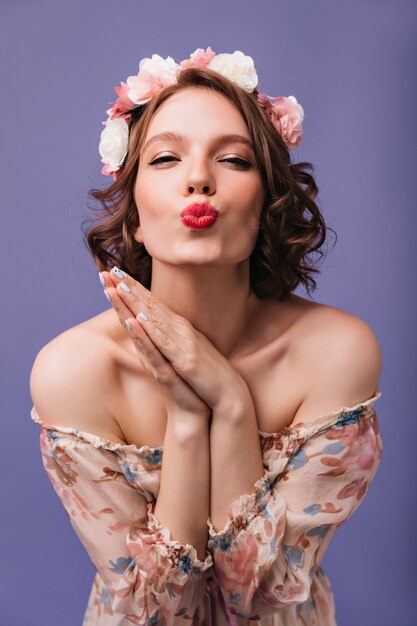 Menina bonita entusiasmada com penteado curto, posando com expressão facial de beijo. Foto interna de uma linda mulher romântica com flores no cabelo isolado.