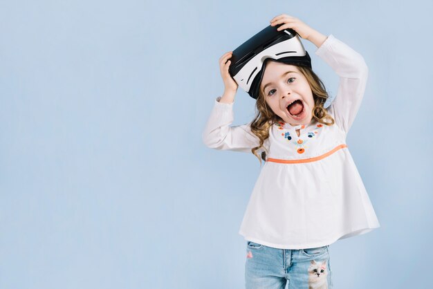 Menina bonita feliz com fone de ouvido virtual na cabeça dela contra o fundo azul