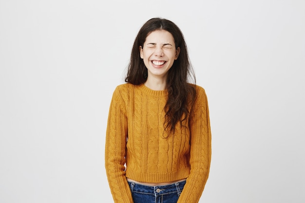 Menina bonita feliz e despreocupada rindo alto com os olhos fechados, ouve uma ótima piada