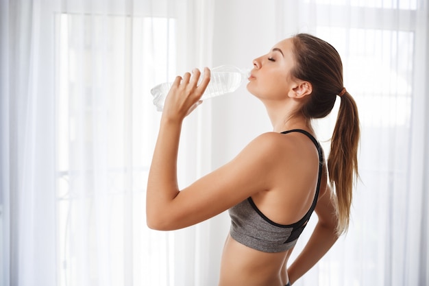 Menina bonita fitness beber água de uma garrafa de plástico