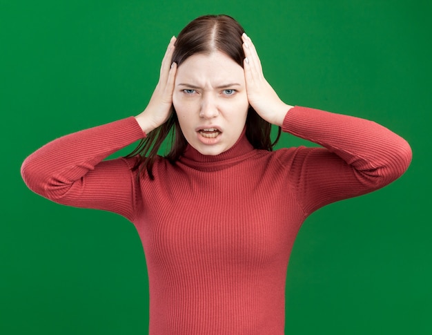 Menina bonita irritada com as mãos na cabeça isolada na parede verde