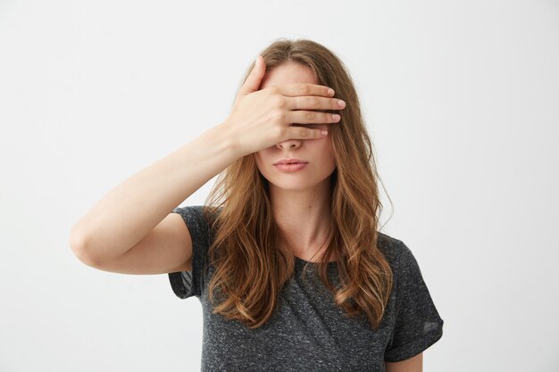 Menina bonita jovem cobrindo fechando os olhos atrás da mão.